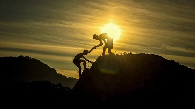 Silhouette of two people climbing a mountain with the sun in the background 